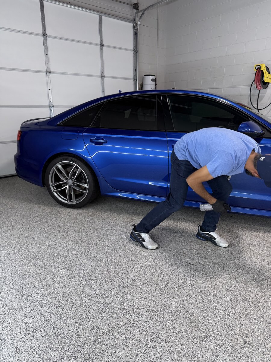 Working down the side of a blue Audi sedan in the shop.