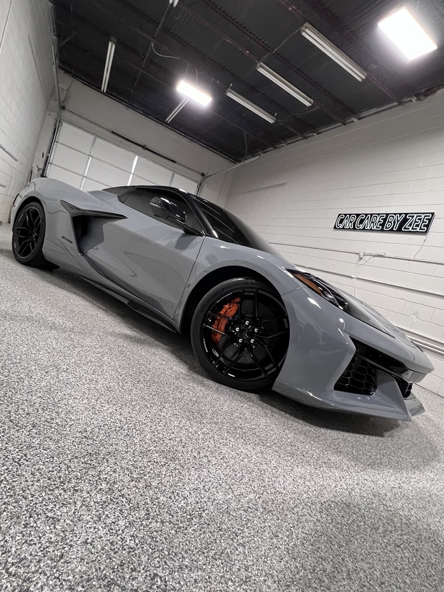 Gray Corvette Z06 under the shop lights, the Car Care by Zee sign on the wall.