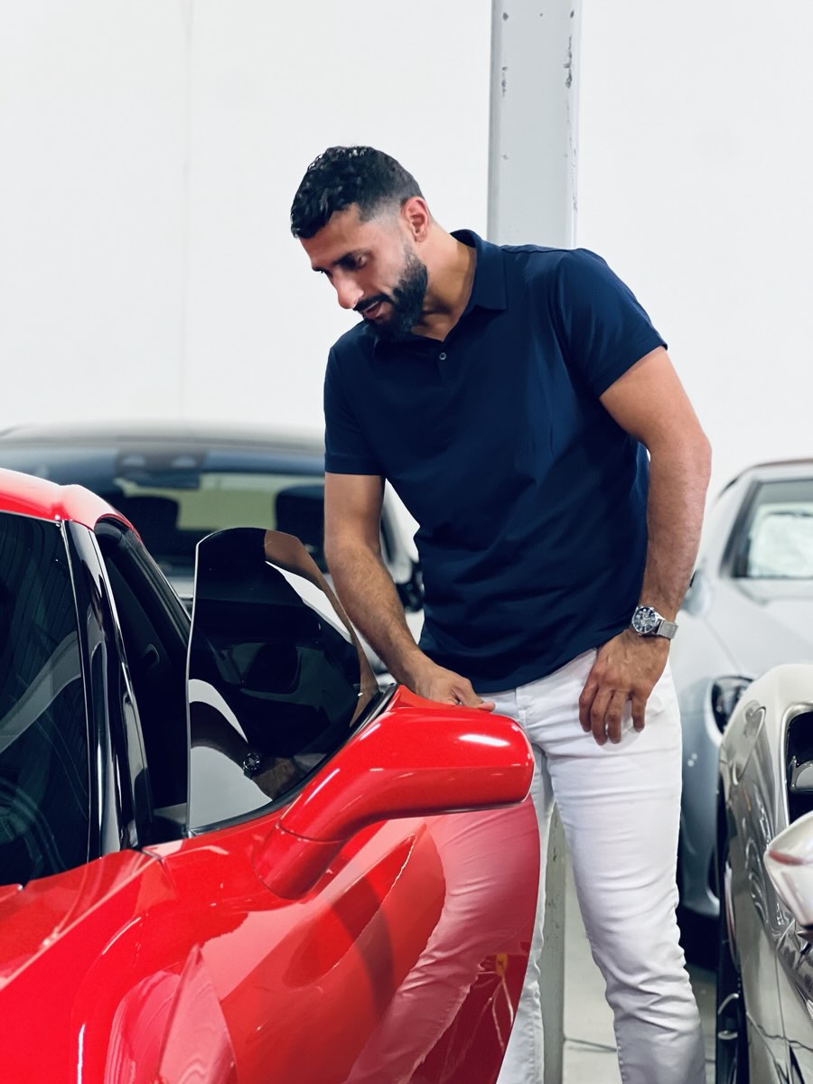 Zee leaning in over the open door of a red Ferrari.