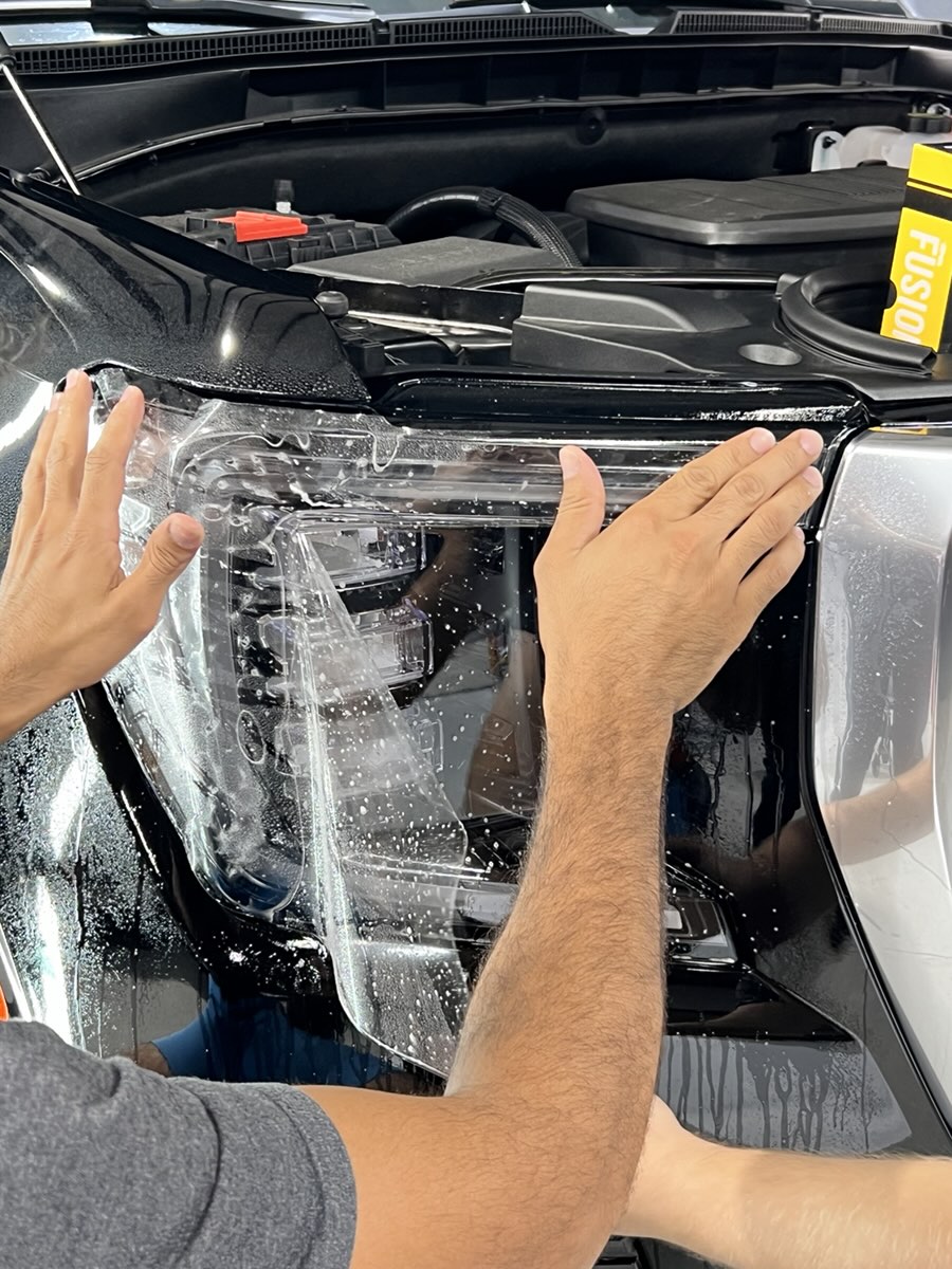 Hands smoothing clear protection film onto a headlight.