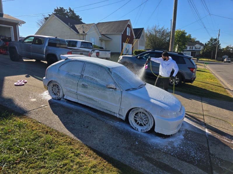White Honda Civic hatchback covered in foam during a mobile detail in a driveway.