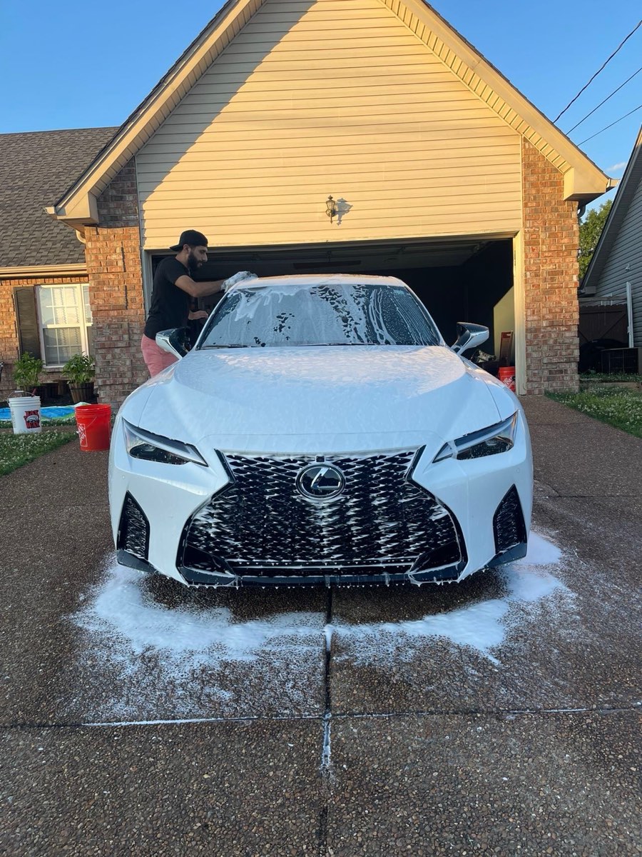 White Lexus IS covered in foam during a mobile detail in a driveway.