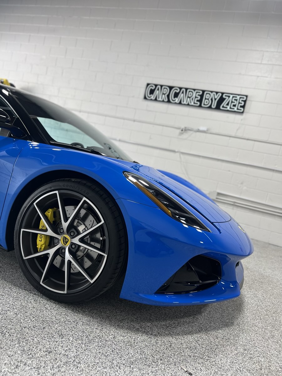 Front wheel and fender of a blue Lotus Emira with yellow brake calipers.
