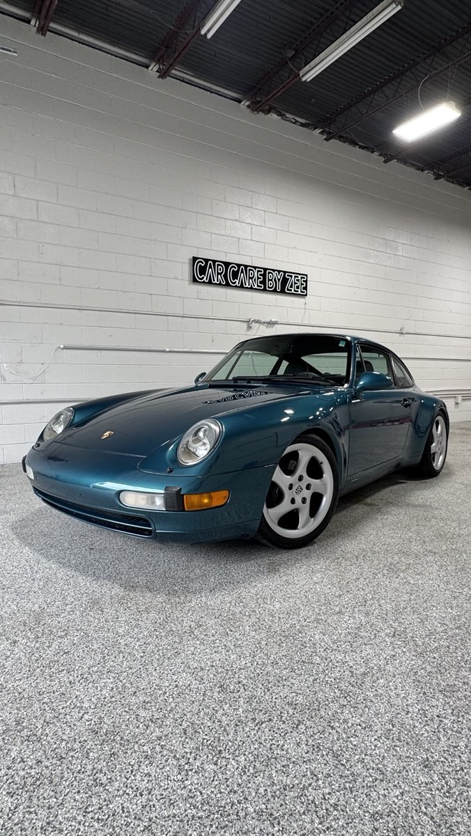 Teal air-cooled Porsche 911 under the Car Care by Zee neon sign in the shop.