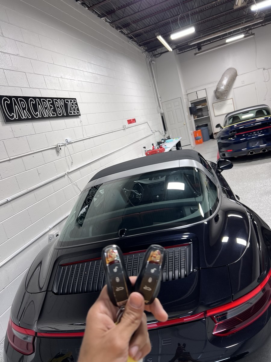 Keys held up behind a black Porsche 911 Targa in the Car Care by Zee shop.