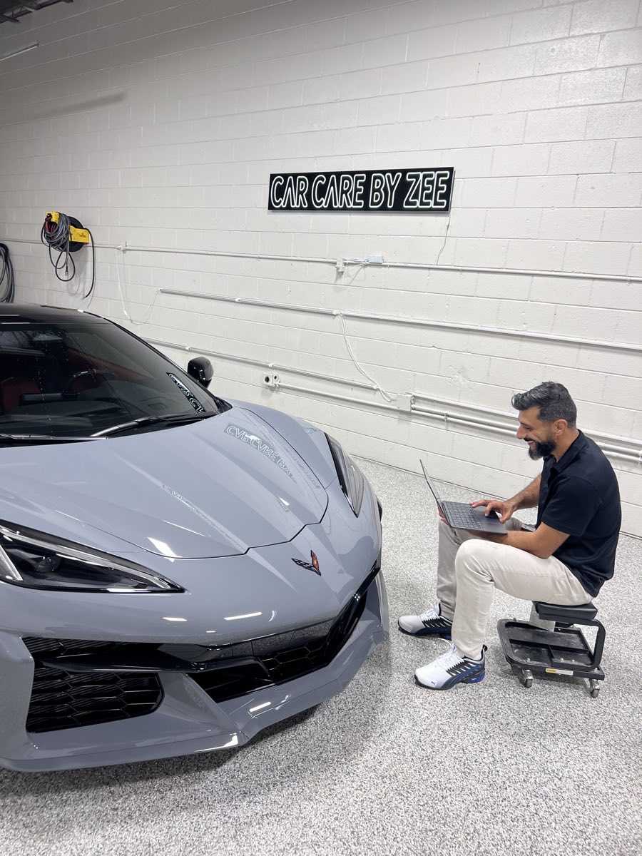 Zee at the Car Care by Zee shop, working on a Corvette under the neon sign.